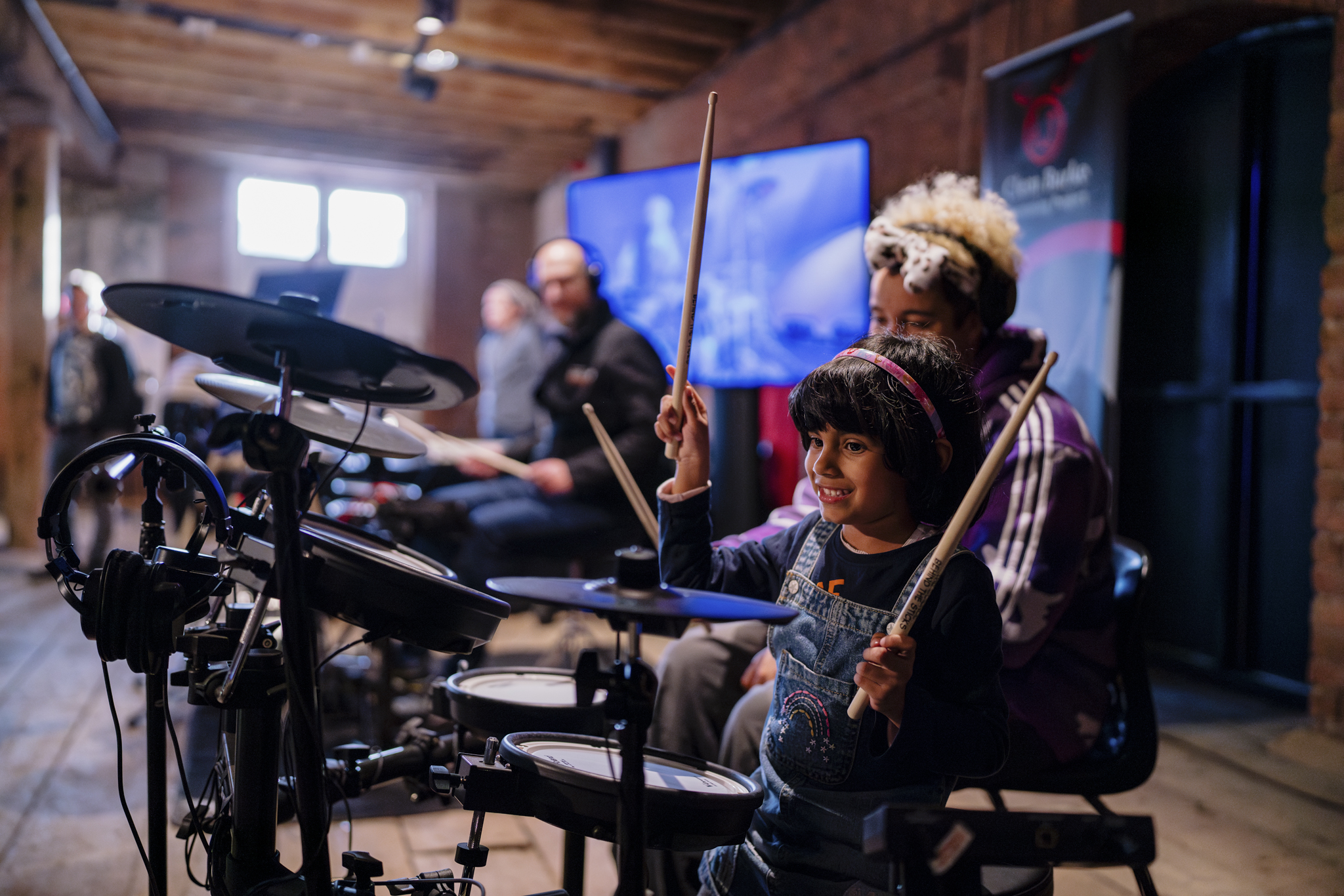 A young girl smiling holding up drumsticks