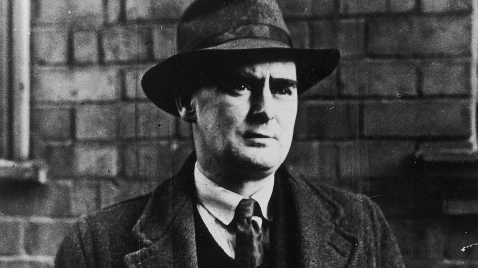 Black and white photograph of Flann O'Brien in long coat and hat