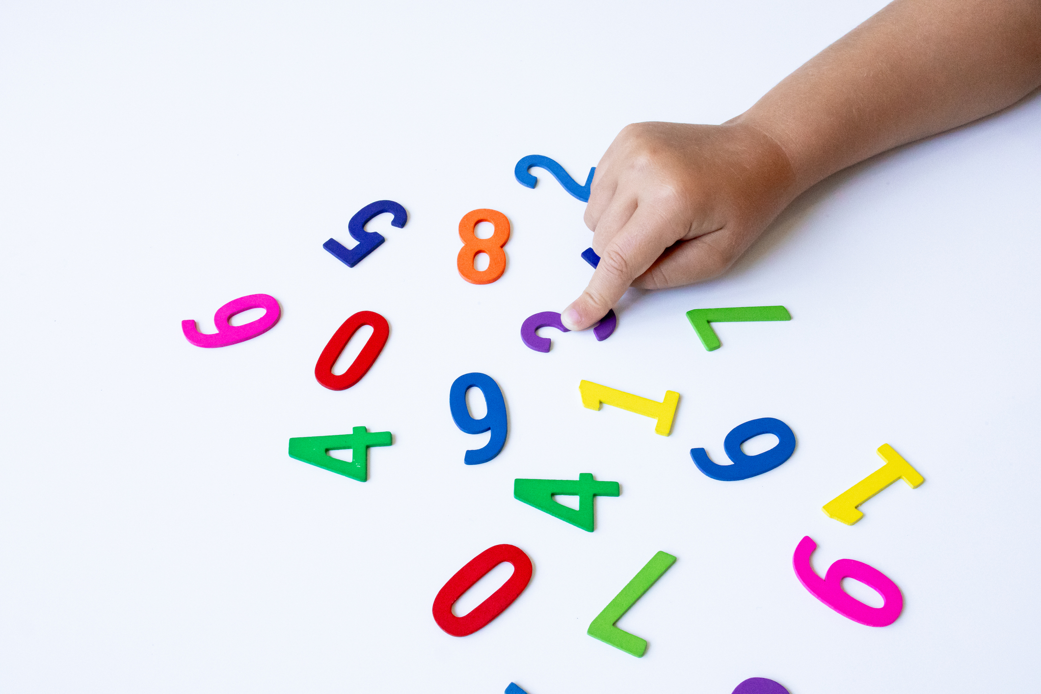 Child hand touching colorful magnetic numbers on white surface. High quality